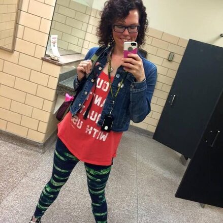 The same woman takes a mirror selfie. Now she wears glasses, a red tee and denim shirt, and striped leggings.